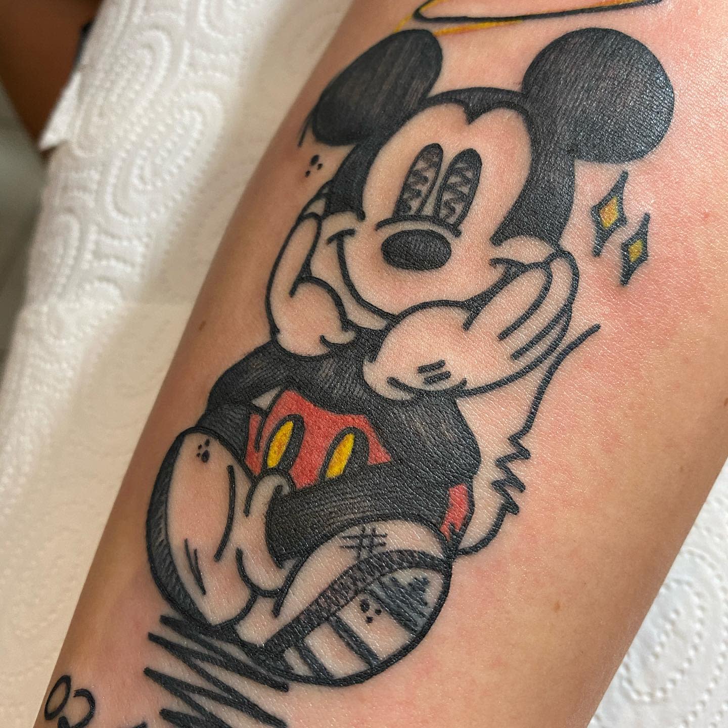 Colorful tattoo of a cute Mickey Mouse sitting with a halo above his head and sparkling eyes