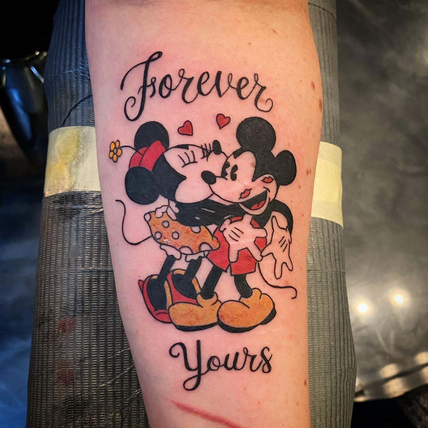 Colorful tattoo of Mickey and Minnie Mouse hugging and kissing, with 'Forever Yours' written above and below