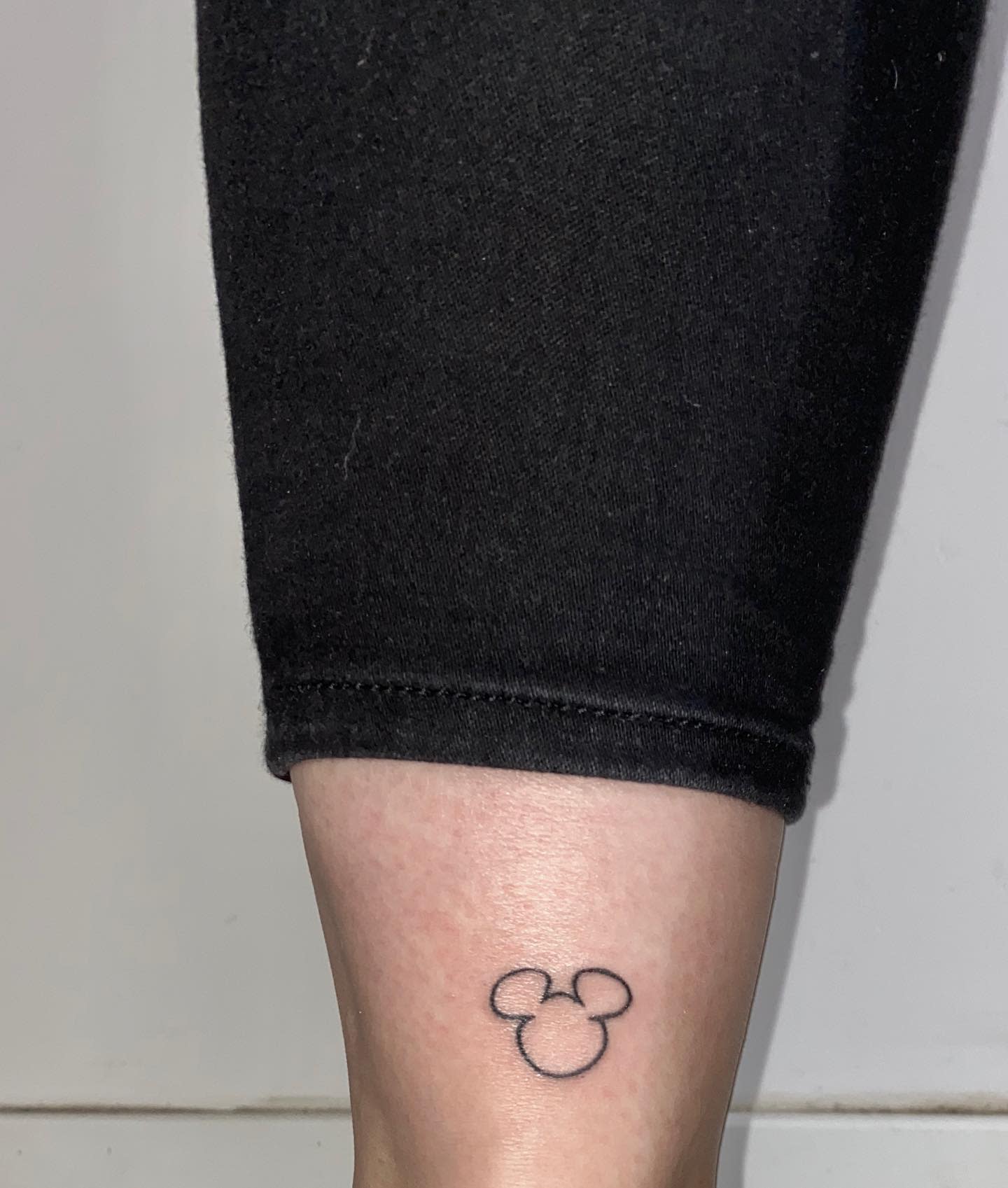 Minimalistic tattoo of a small outline of Mickey Mouse's head placed on the lower leg