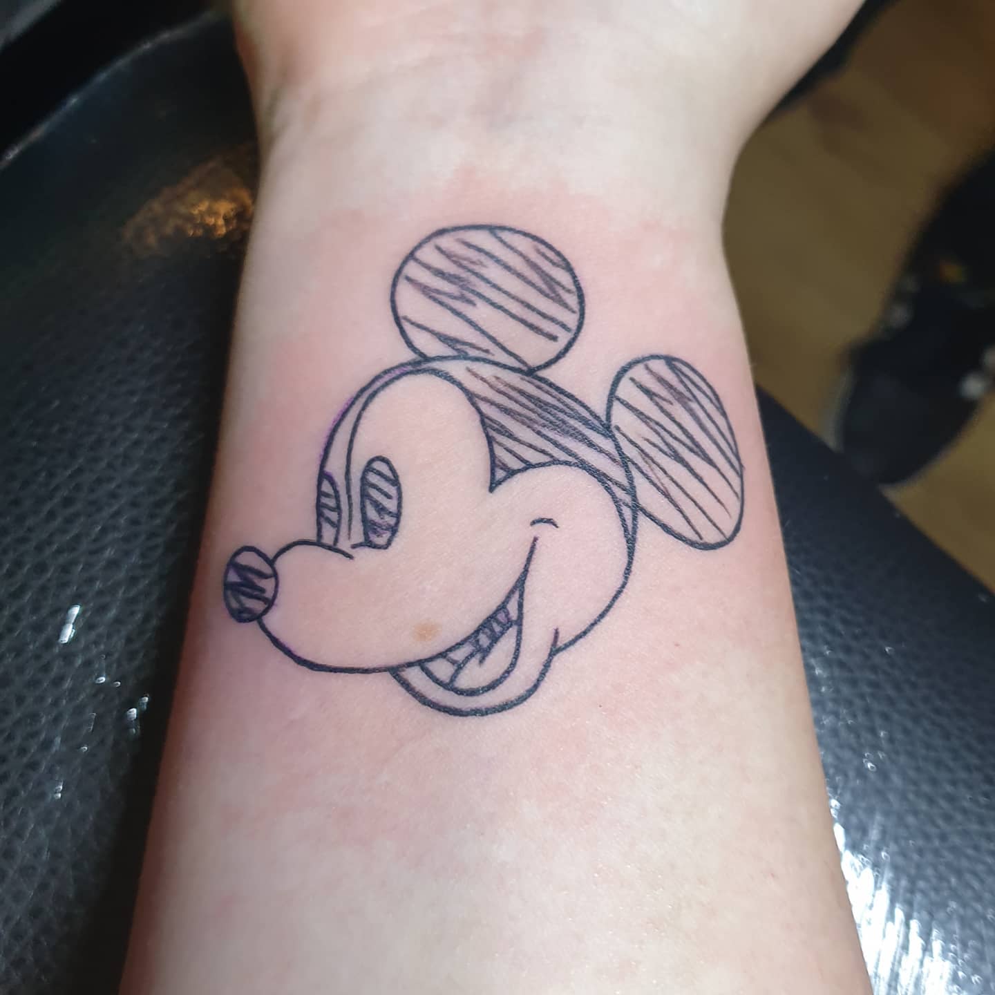 Tattoo of a sketch-style outline of Mickey Mouse's face, with hatched shading on the ears and eyes