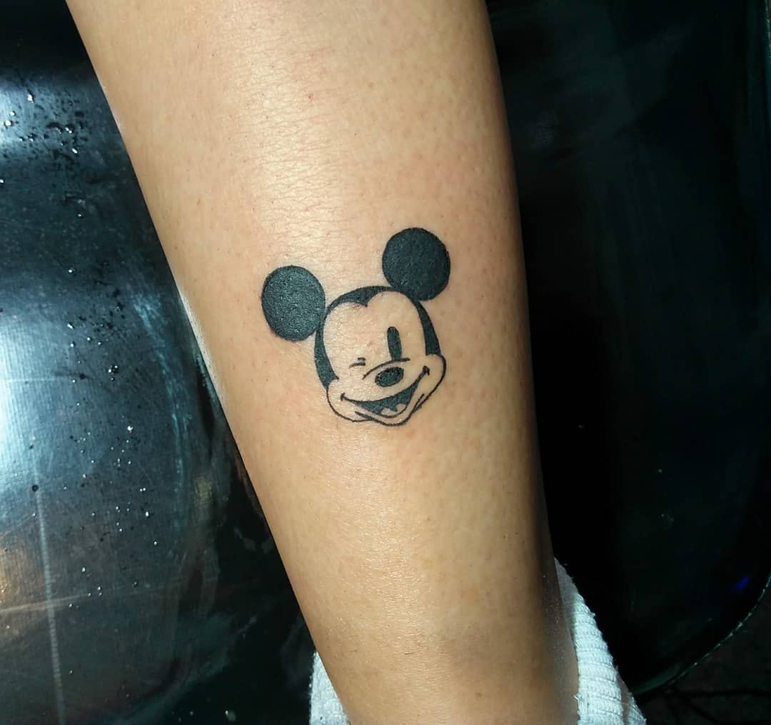 Small tattoo of Mickey Mouse's face winking, with solid black ears, placed on the lower leg