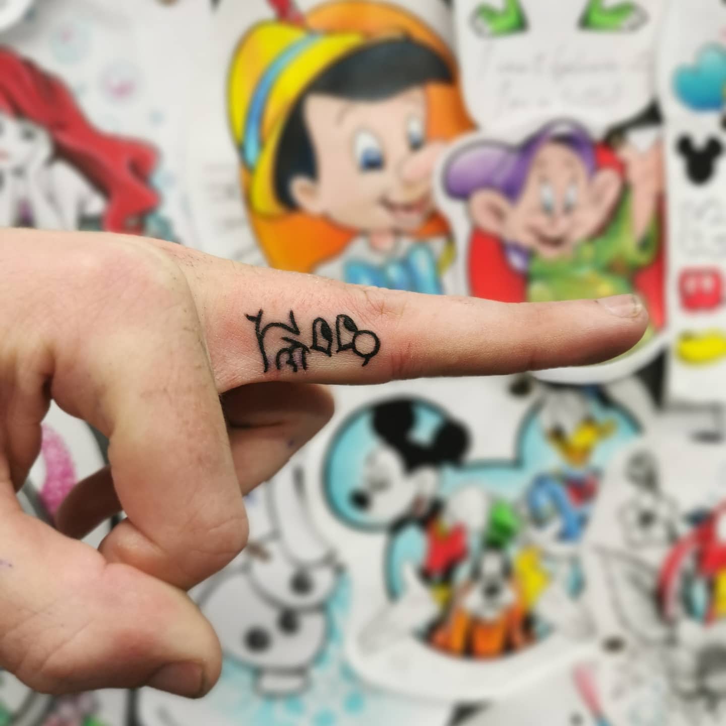Small tattoo of Mickey Mouse's head outline incorporated into the word 'Hello,' placed on a finger.
