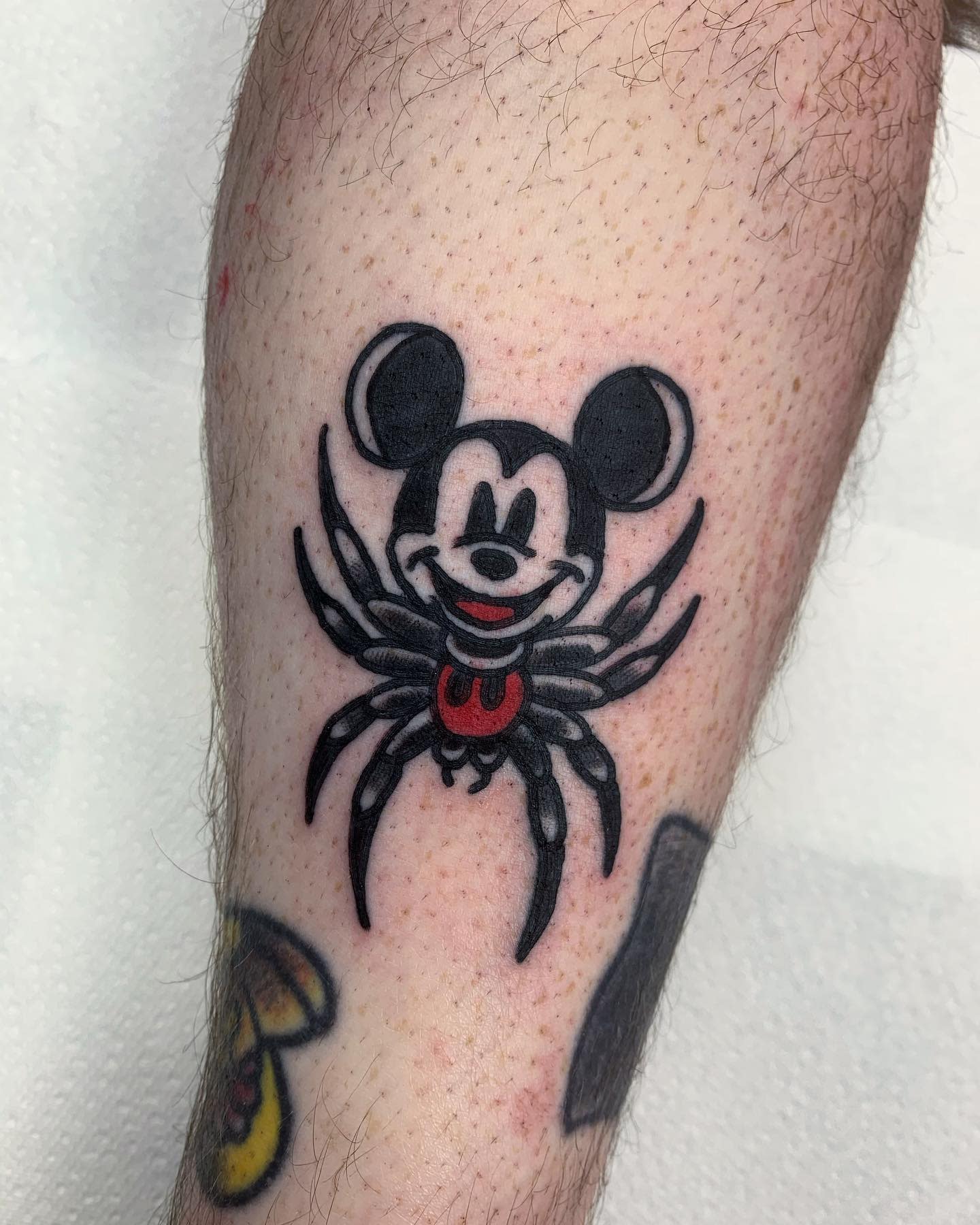 A tattoo of Mickey Mouse with a spider body on someone's leg