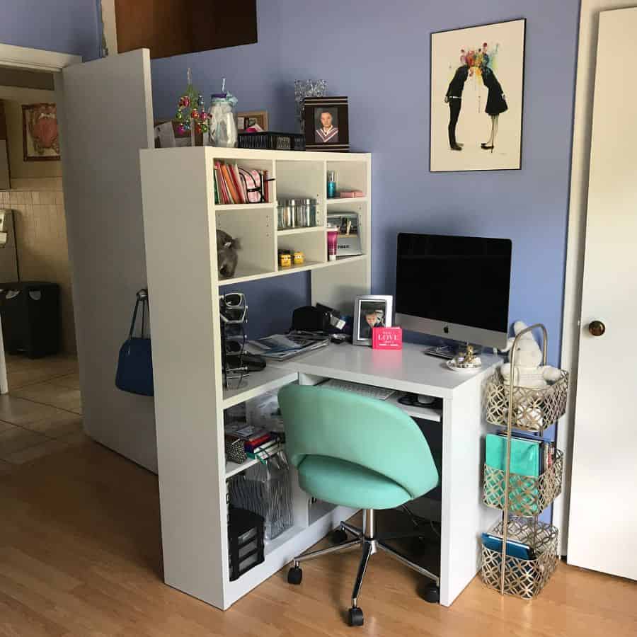 Home office with white desk and shelves, teal chair, desktop computer, and decorative items in a cozy room
