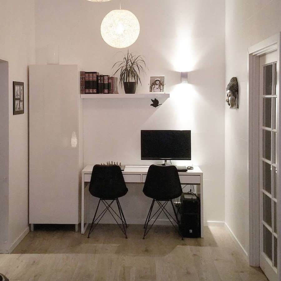 Minimalist home office with a desk, two chairs, a computer monitor, and shelves with decor and books
