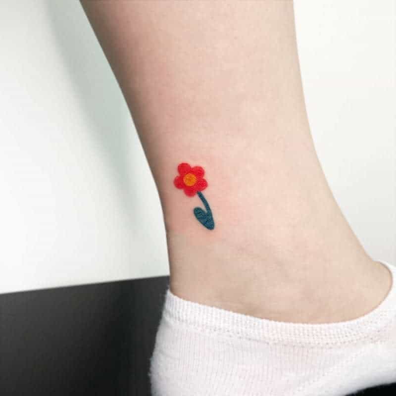 A small red flower tattoo on an ankle