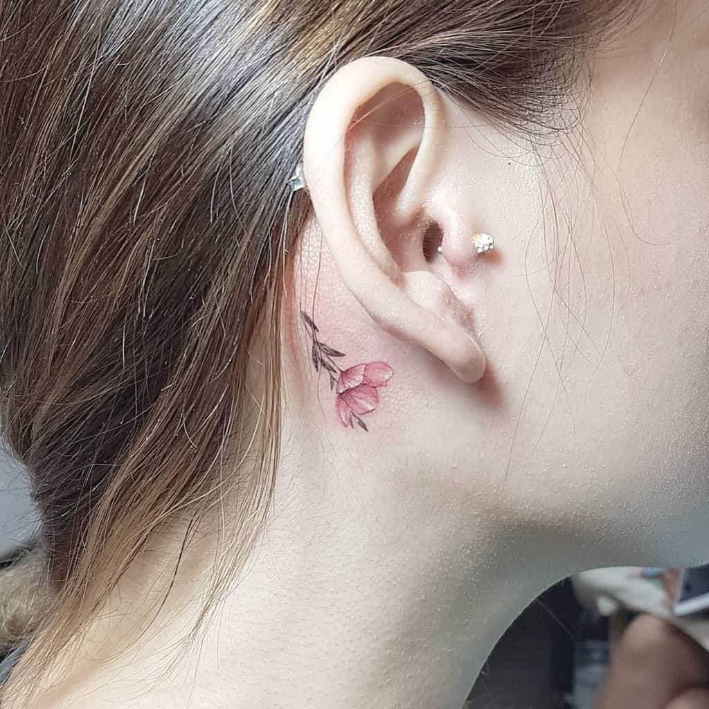 Small pink flower tattoo behind an ear