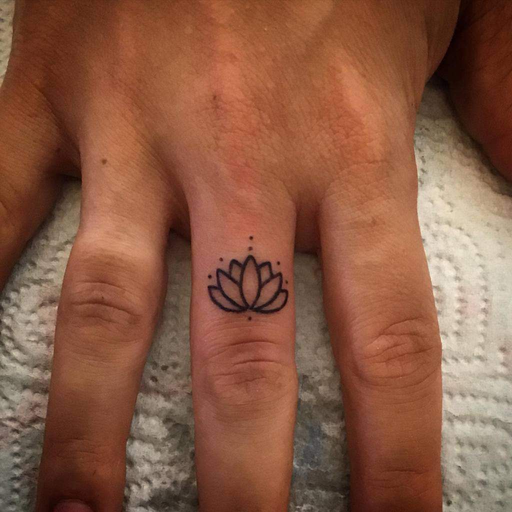 Lotus flower tattoo on the ring finger of a hand resting on a textured surface