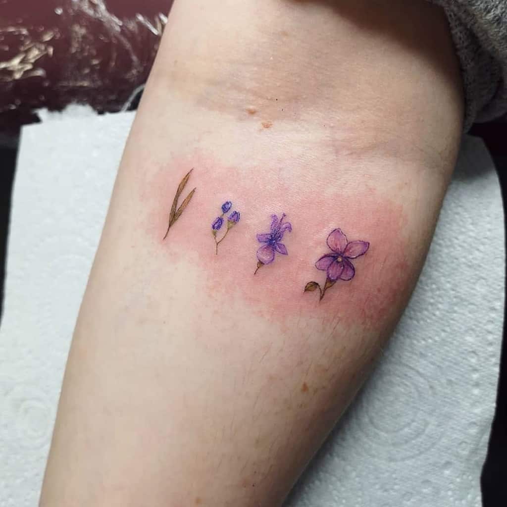 Small tattoo of violet flowers and leaves on a forearm