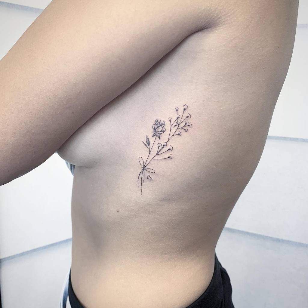 A delicate floral tattoo on a person's side, featuring a rose and small buds in a minimalist design