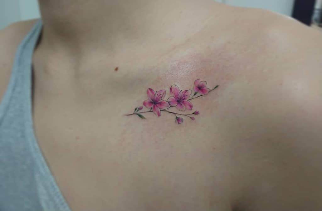 A delicate pink cherry blossom tattoo near the collarbone