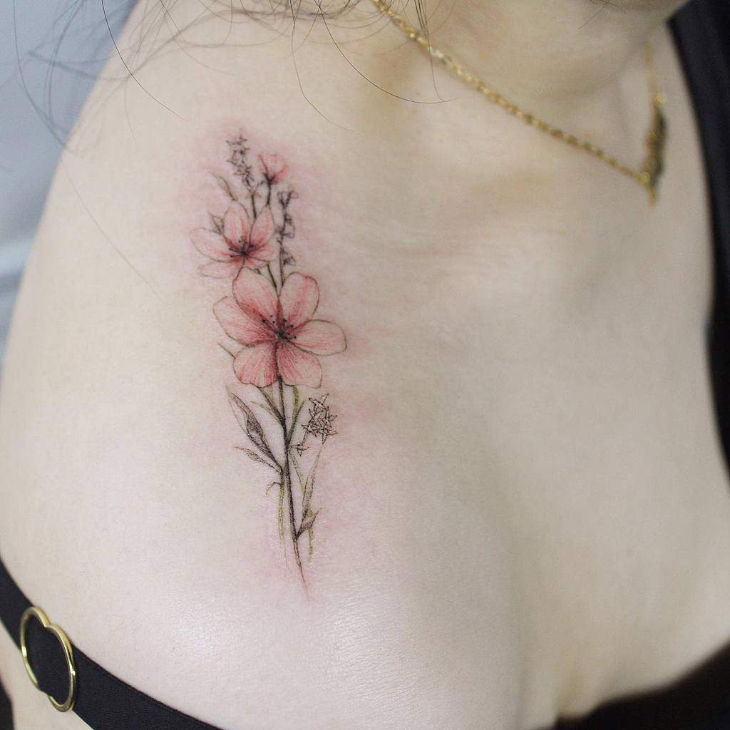 A delicate pink floral tattoo on a woman's shoulder