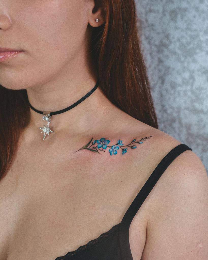 A woman has a blue flower tattoo on her collarbone