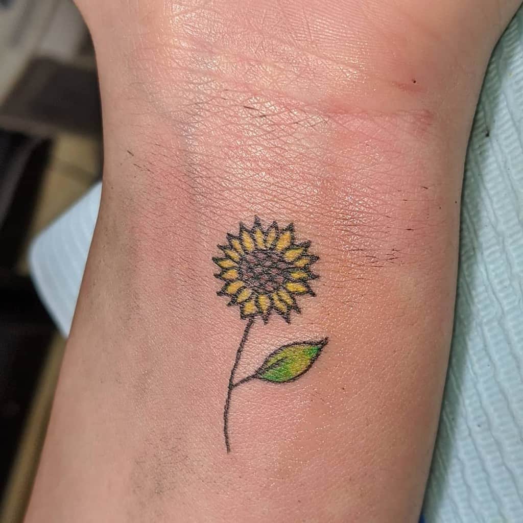 A small sunflower tattoo on a wrist, featuring a yellow bloom and a single green leaf