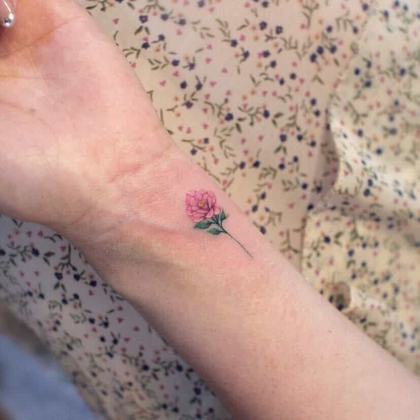 A small pink rose tattoo on a person's wrist