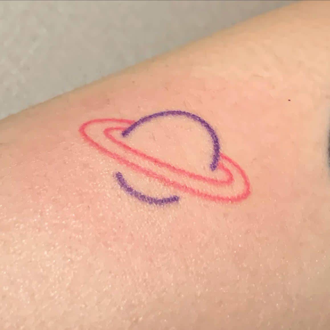 Tattoo of a purple Saturn planet and red rings on a forearm