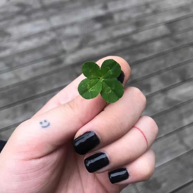 A small smiley face tattoo on the finger with a red line ring tattoo