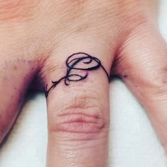 A minimalist ring tattoo featuring a swirling, elegant line that forms a decorative letter "C" with a vine-like flourish