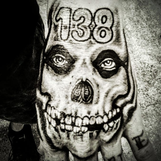 Black and white tattoo of a skull with the number 138 on a hand