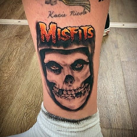 Tattoo of a skull and the word "Misfits" above it on a leg