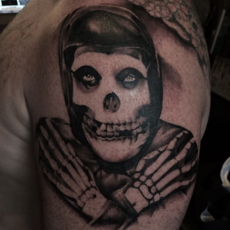 Tattoo of a hooded skeleton with crossed arms on an upper arm