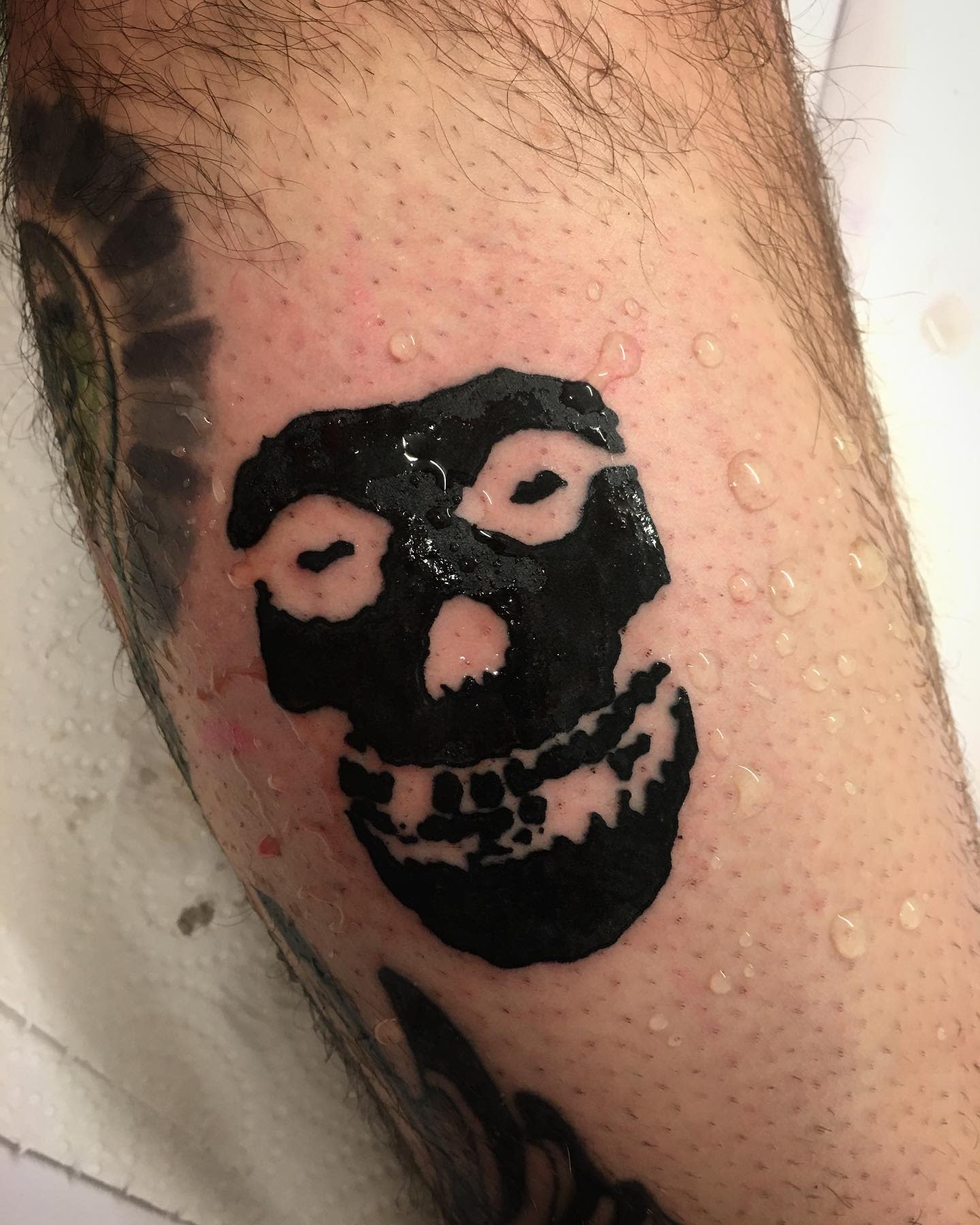 Fresh black skull tattoo on a leg with water droplets on the skin