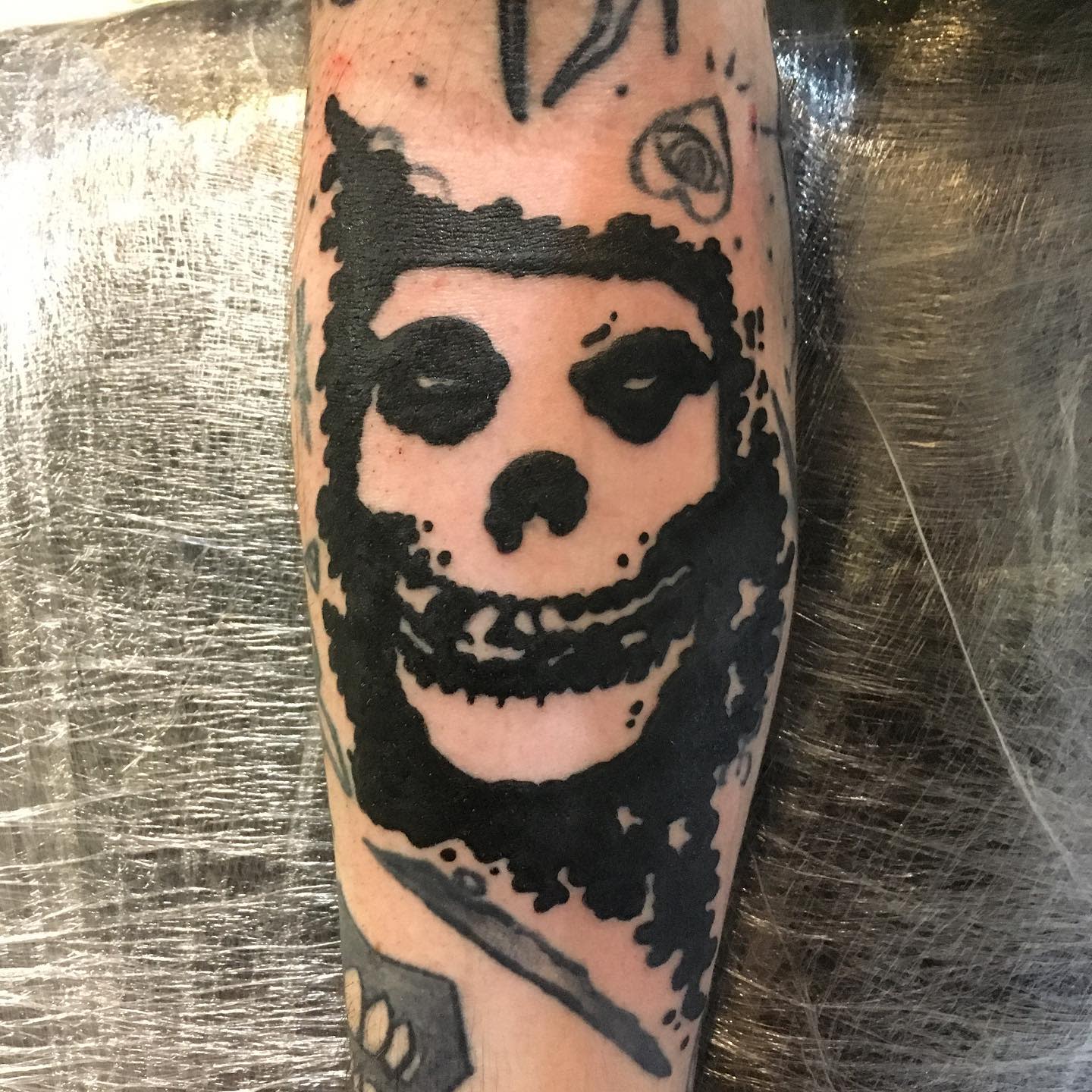 Black tattoo of a circular skull with dark eyes and a broad grin on a forearm