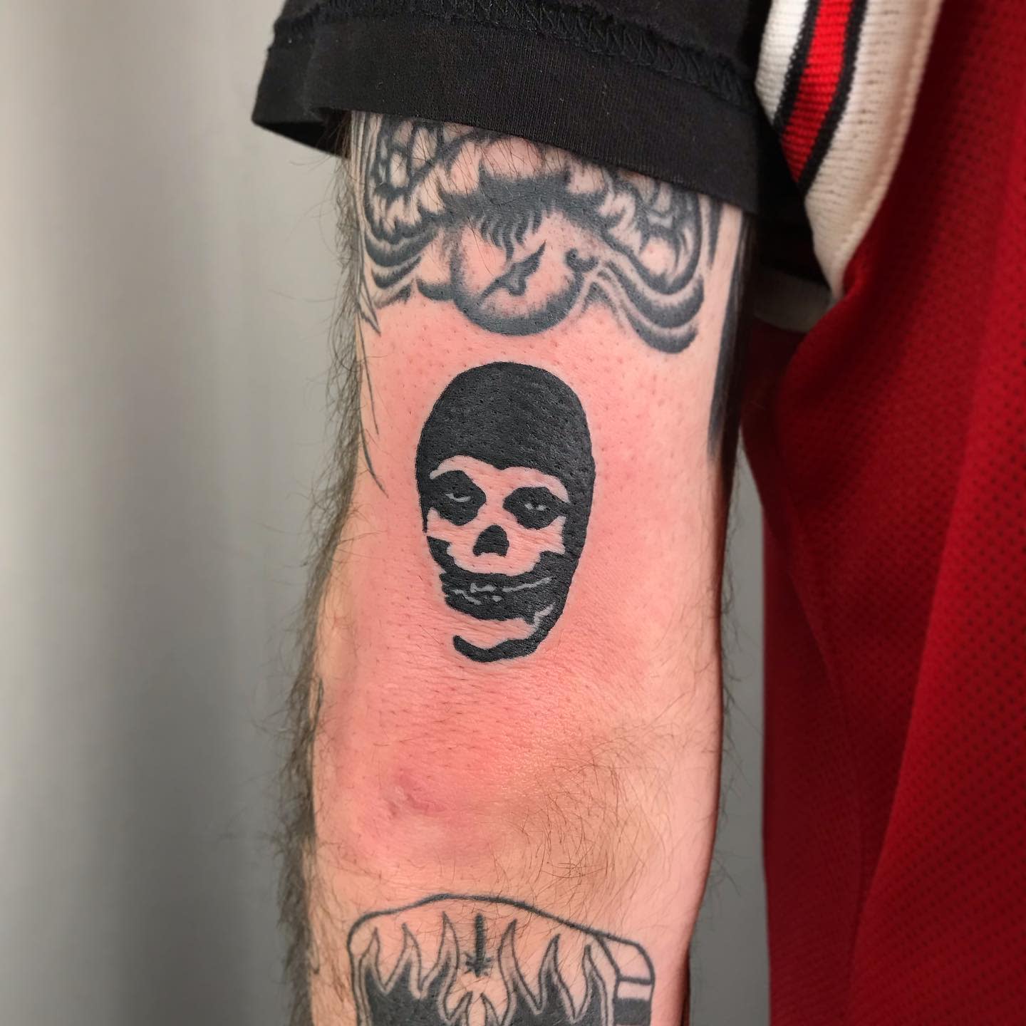Tattoo of a skull face on an arm with other tattoos visible