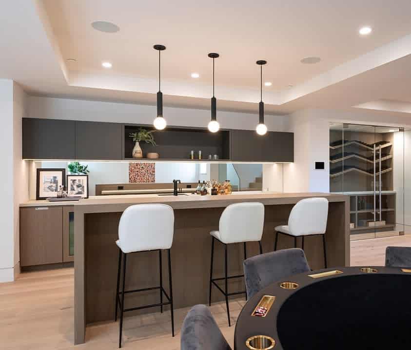 Modern kitchen bar with minimalist pendant lights, white stools, and sleek cabinetry.