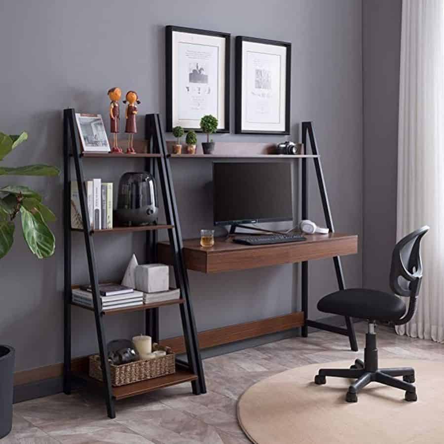 Modern home office with a wooden desk, black chair, shelves, plants, and framed art on a gray wall