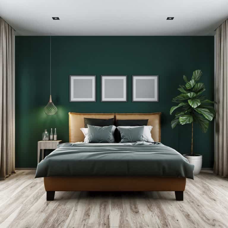 Modern bedroom with green walls, framed art, pendant light, potted plant, and a bed with gray and beige bedding