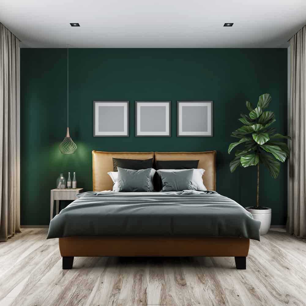 Modern bedroom with green walls, framed art, pendant light, potted plant, and a bed with gray and beige bedding