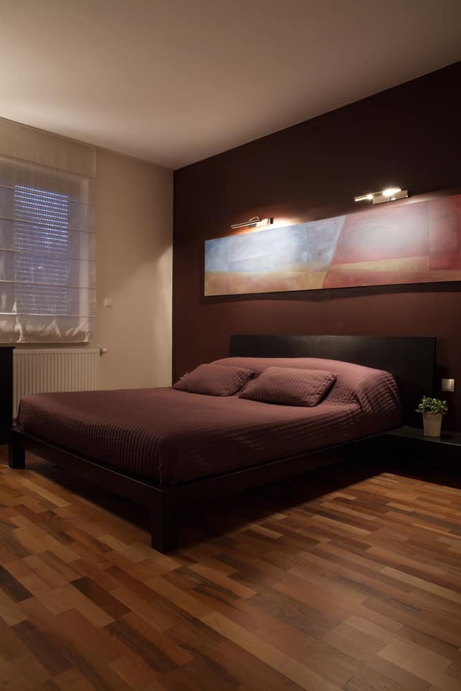 Modern bedroom with dark accent wall abstract art and minimalist wall sconces.