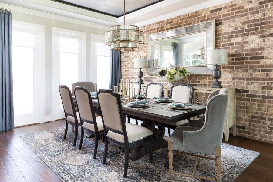 exposed brick accent wall long dining table and chairs wall mirror elaborate chandelier