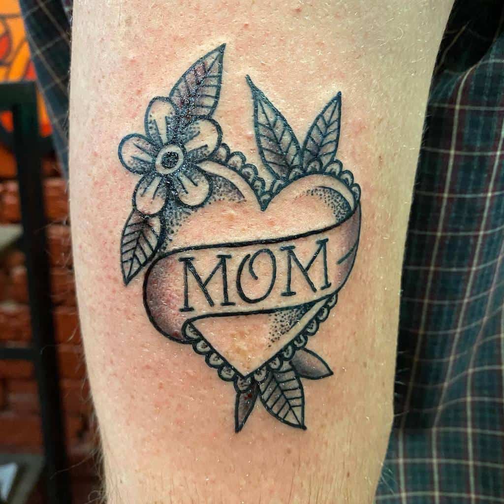 A heart tattoo on an arm, featuring the word "MOM" inside, adorned with delicate leaves and a blooming flower