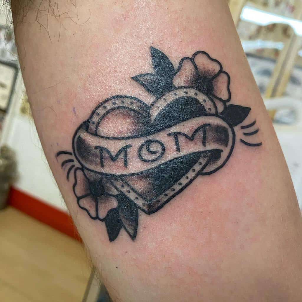 Tattoo of a heart with "MOM" written across it, elegantly adorned with flowers