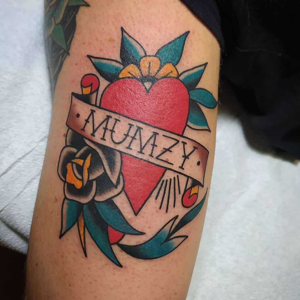 Tattoo of a red heart with "MUMZY" banner, surrounded by flowers and leaves, celebrating the essence of mom