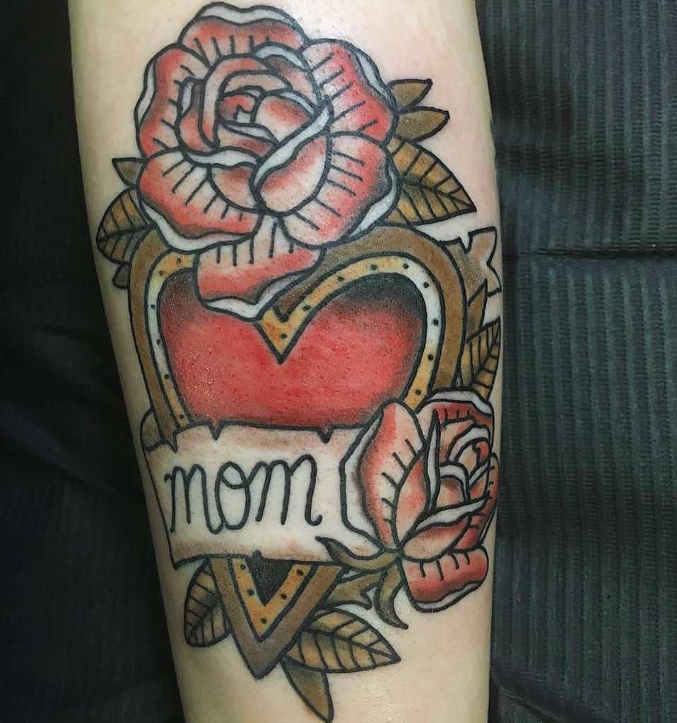 A tattoo of a heart framed by roses, with an elegant banner that proudly says "mom" on a person's forearm