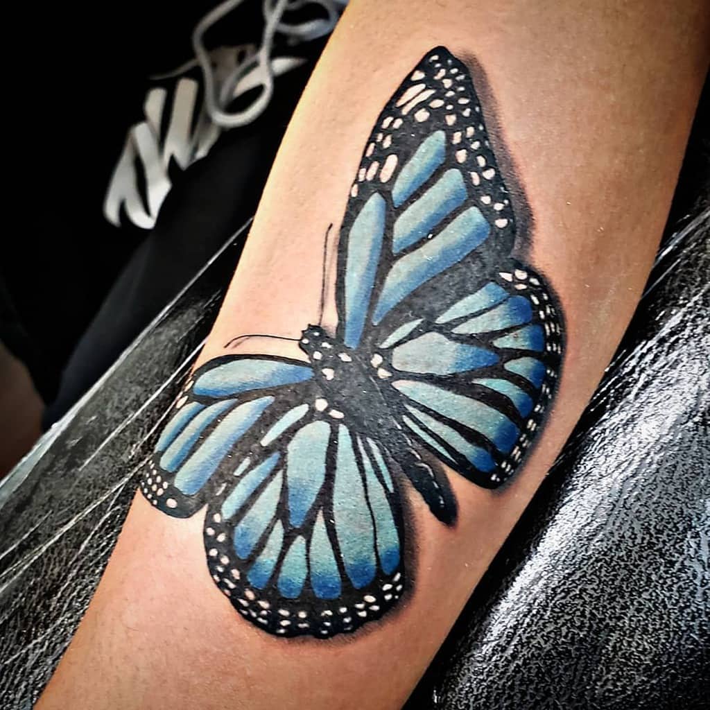 A stunningly realistic blue butterfly tattoo is beautifully inked on an arm