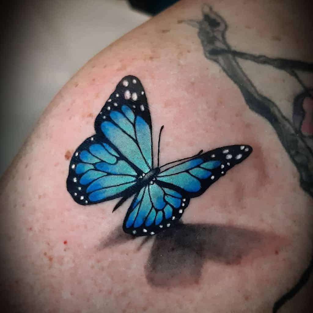 A captivating blue butterfly tattoo graces a person's skin, its delicate wings artistically blending over an older design