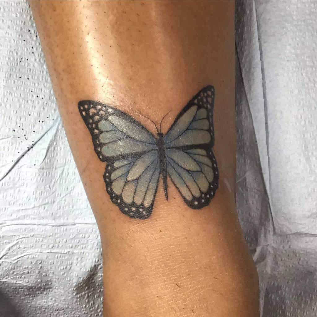 A striking blue butterfly tattoo elegantly adorns a person's leg, capturing intricate details with realistic precision