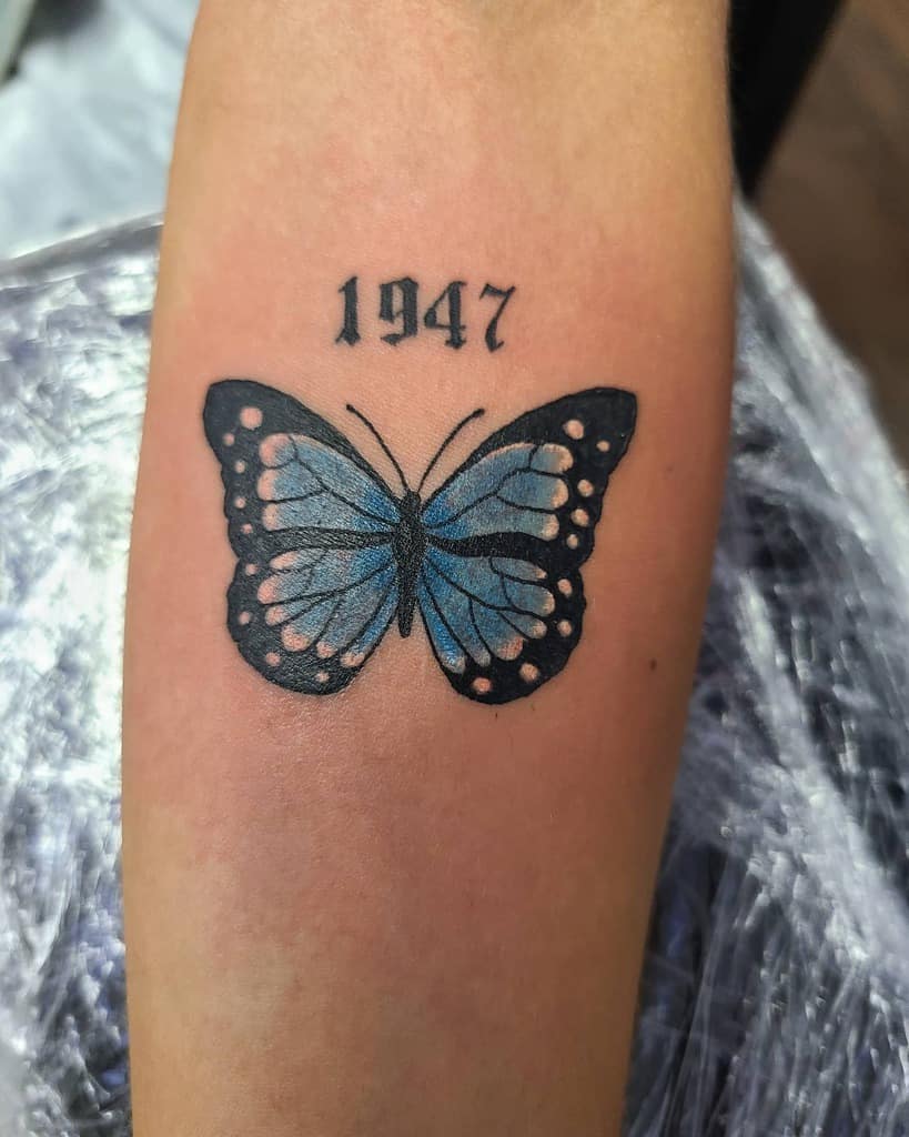 Tattoo of a delicate blue butterfly with the year "1947" inked above it