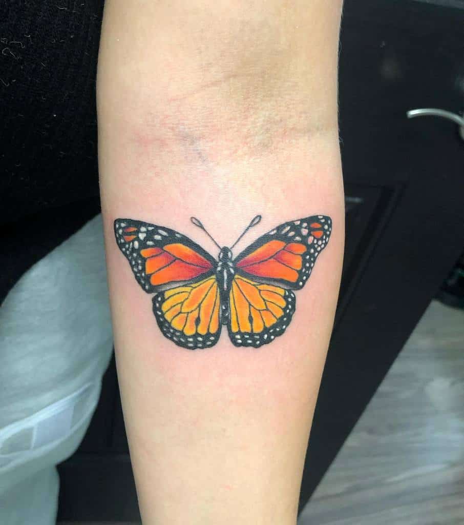 A vibrant monarch butterfly tattoo on a forearm, its orange and black wings intricately detailed