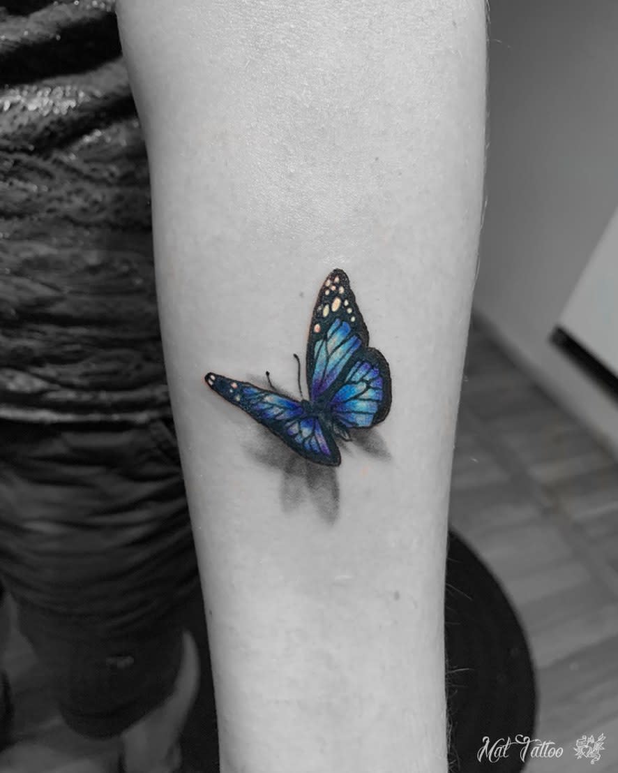 A realistic blue monarch butterfly tattoo on a forearm