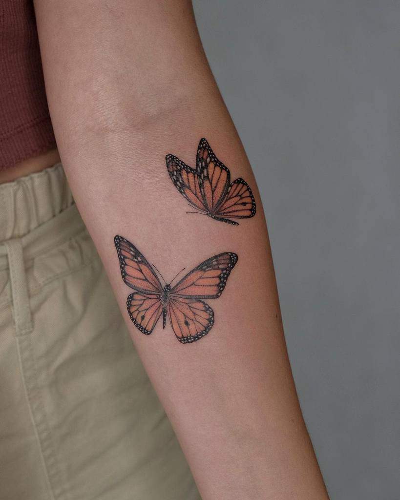A pair of vividly detailed monarch butterfly tattoos adorn a forearm