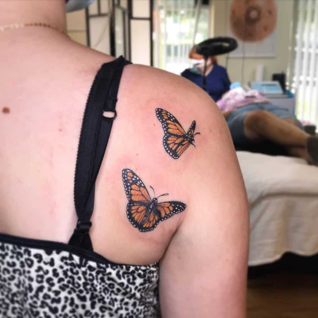 A pair of stunning monarch butterfly tattoos grace a woman's upper back and shoulder