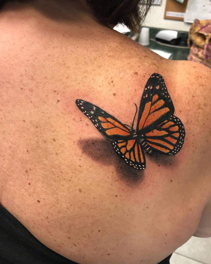 A stunning tattoo featuring a vividly colorful monarch butterfly on a woman's upper back, capturing the essence of nature's elegance