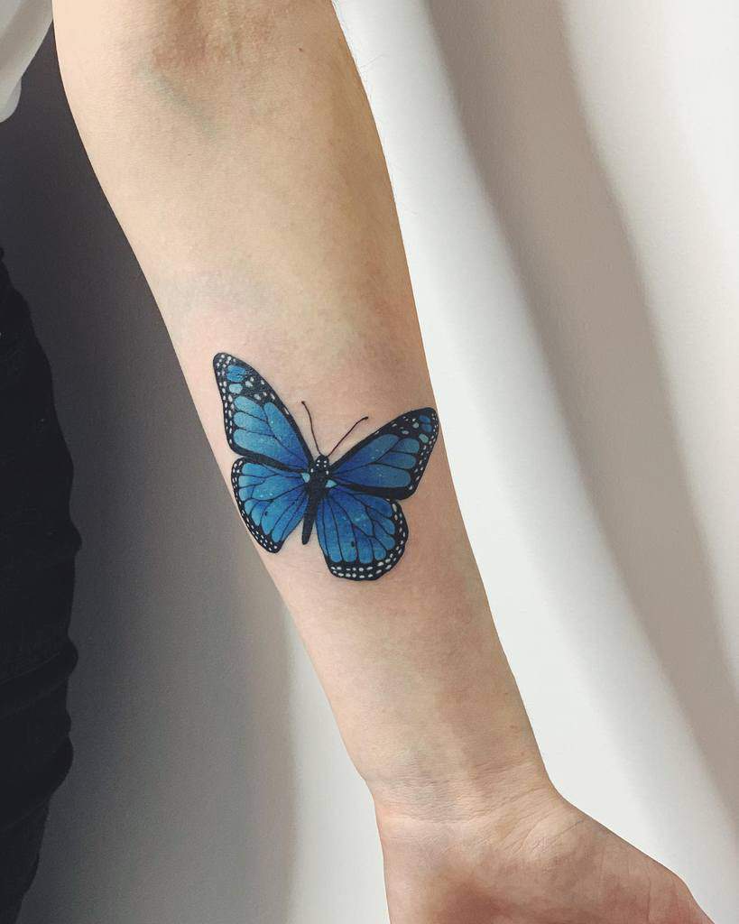 Vibrant blue butterfly tattoo on the forearm, featuring detailed shading and fine black outlines for a realistic and elegant design.
