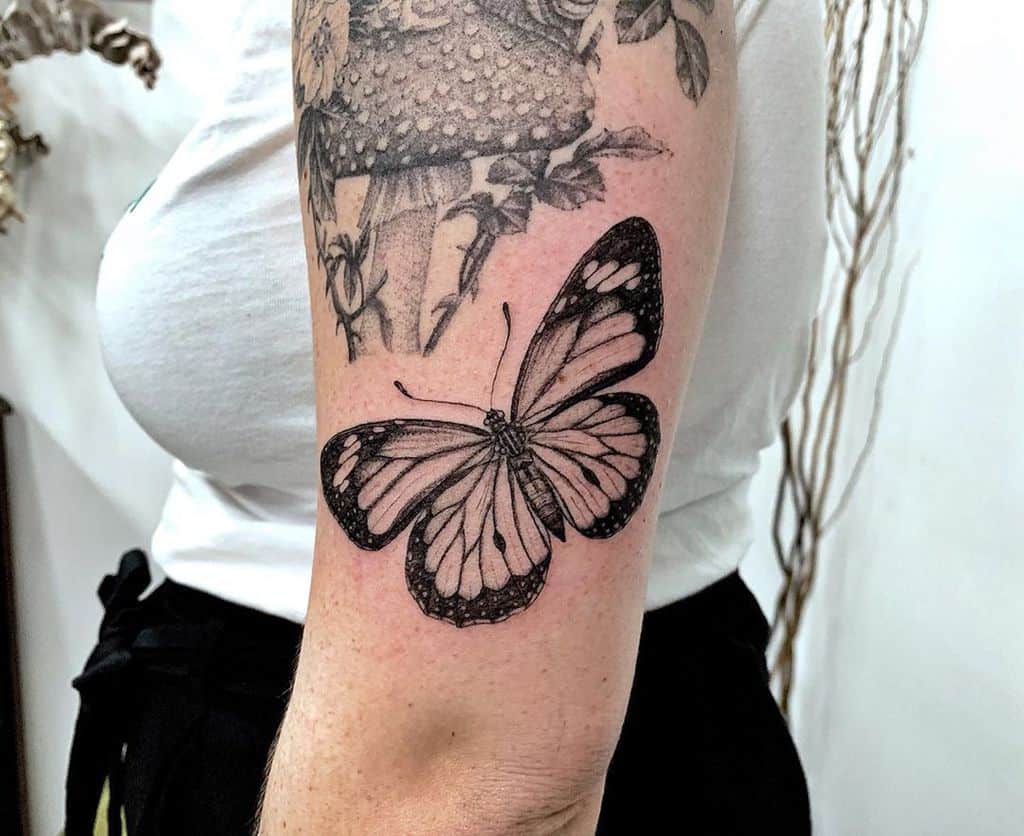 A black monarch butterfly tattoo graces a person's arm next to a delicate floral design