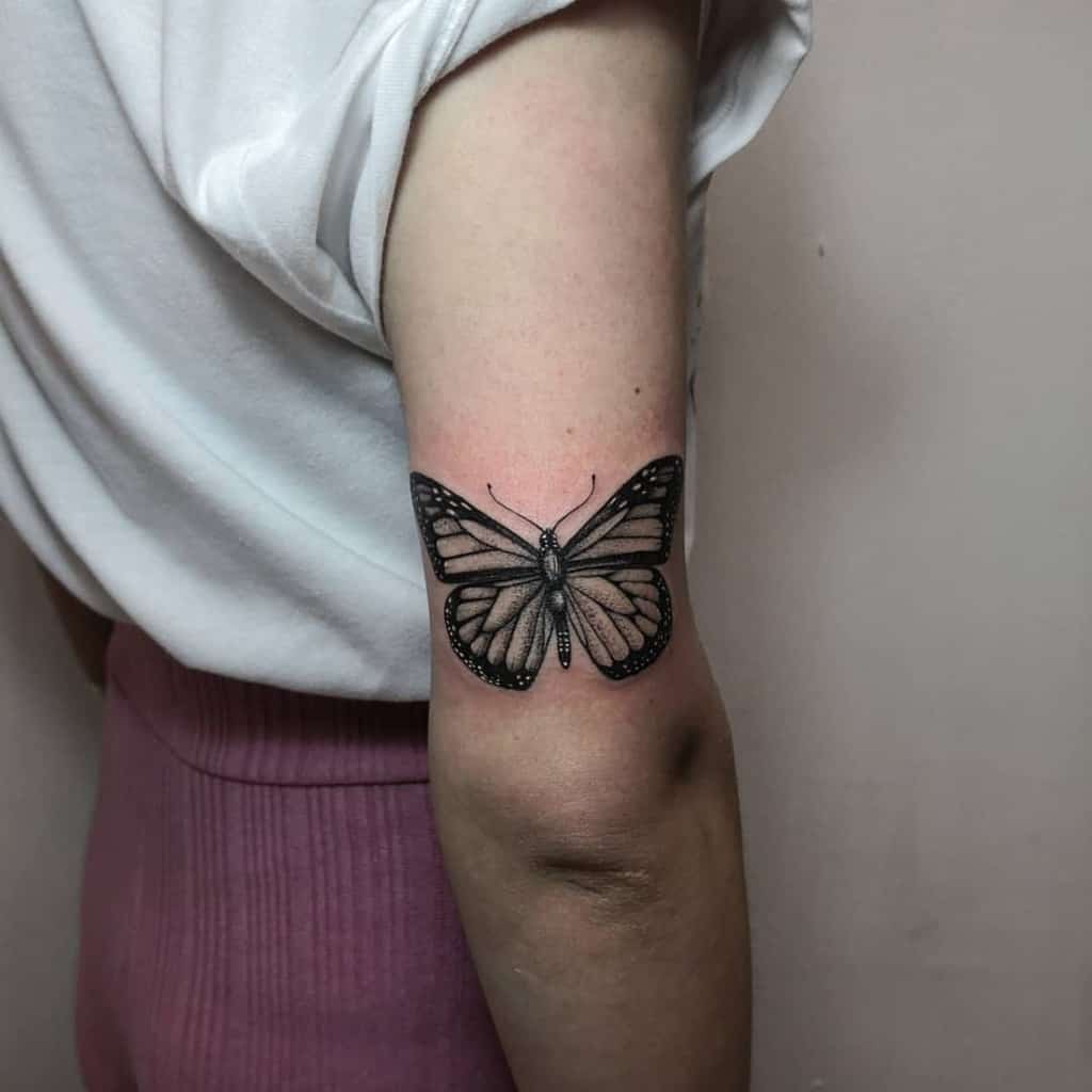 A detailed black monarch butterfly tattoo graces a person's arm above the elbow